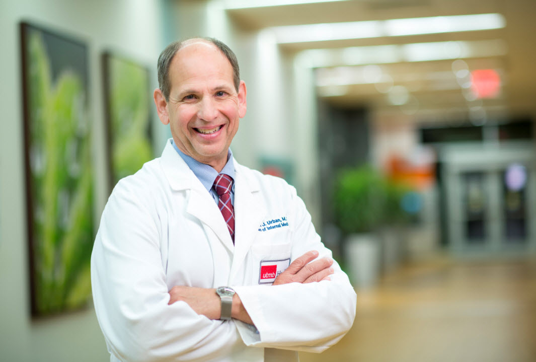 Dr. Randall Urban stands in a hallway of a hospital wearing his white coat