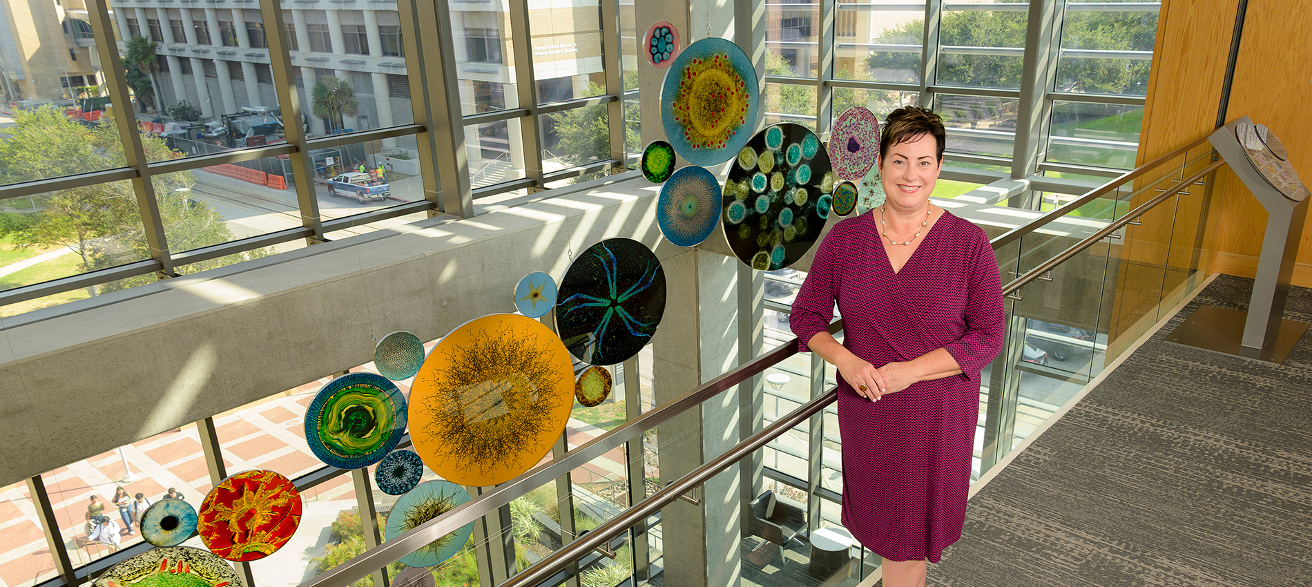 Kristen Starnes-Ott, wearing a wine-colored dress, poses in front of an art installation of colorful round glass pieces.