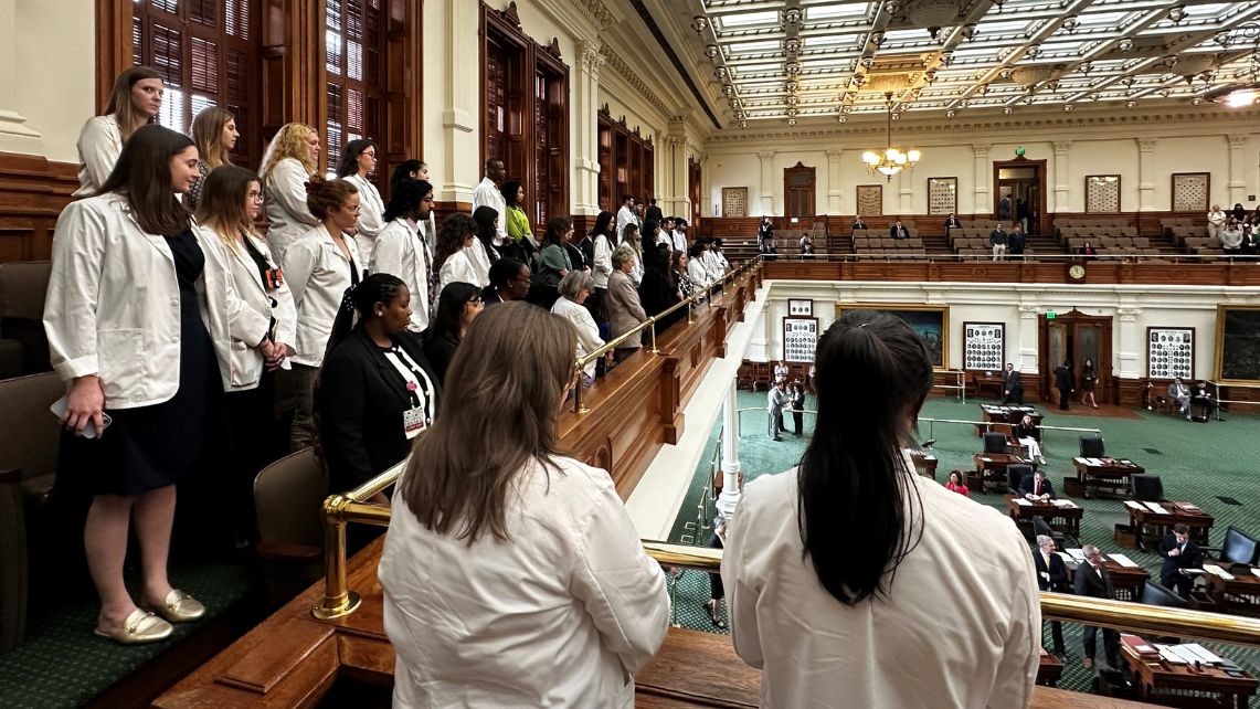 Group of UTMB students standing along a balcony railing inside the Texas House chamber, overlooking the legislative floor during a visit to the State Capitol
