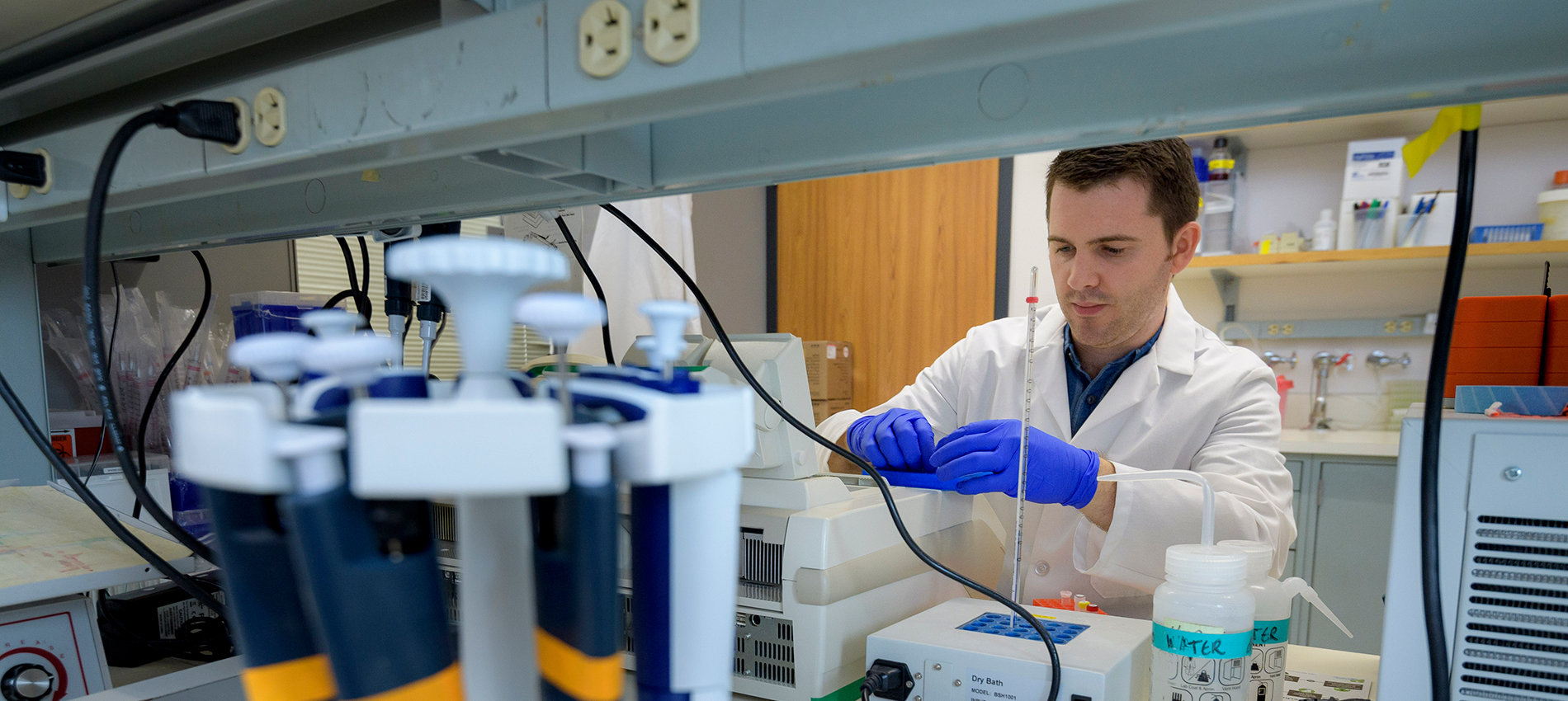 A man in a white lab coat and blue gloves sets up for an experiment in a lab at UTMB.