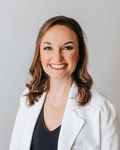 Taylor Little, FNP Professional headshot of a person wearing a white coat over a dark top, facing the camera against a light gray background.
