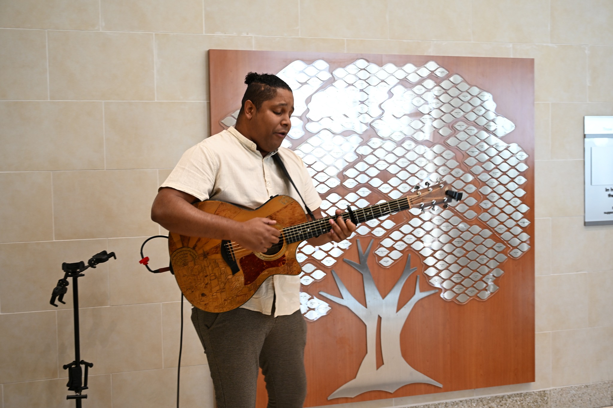A musician plays an acoustic guitar in the Jennie Sealy Hospital lobby while standing in front of the Tree of Life wall display, which honors organ donors and transplant recipients at UTMB