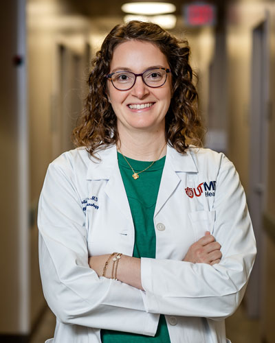 Dr. Julia W. Tripple Person in a white clinical coat stands in a hallway with arms crossed. A UTMB Health logo is visible on the coat.