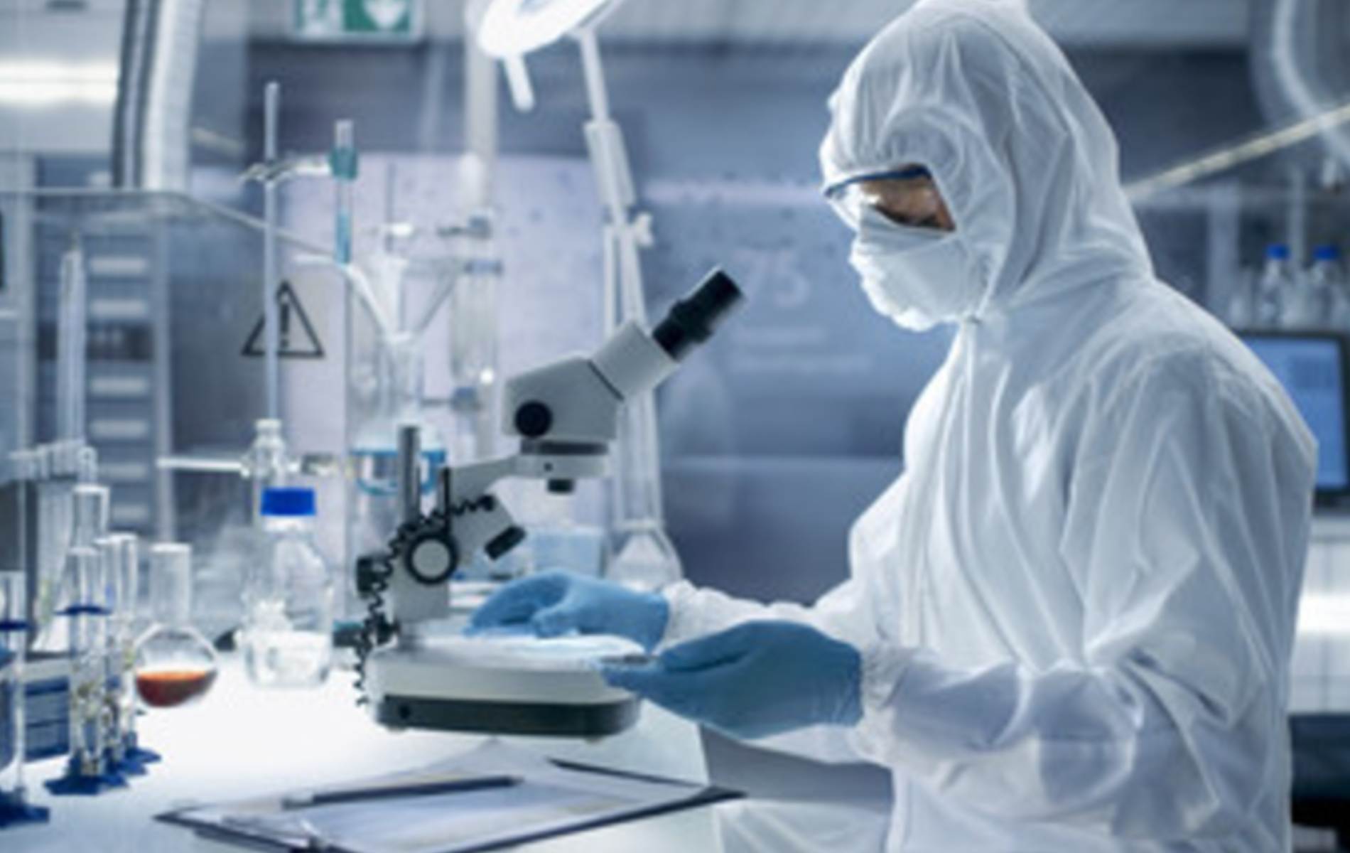 Medical professional in protective gear in lab looking through microscope