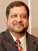 In a head-and-shoulders photo, a man with short dark hair is wearing a brown suit and tie with a white shirt.