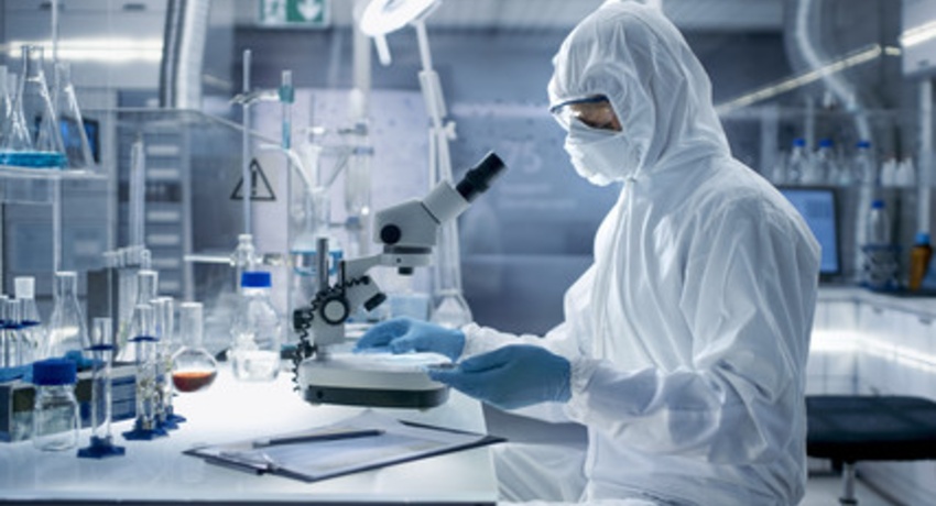 Medical professional in lab with protective gear looking in microscope