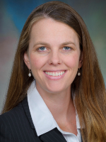 Dr. Amy Kreykes A professional headshot of a woman with long straight brown hair, blue eyes, and a warm smile, wearing a dark blazer over a white collared shirt against a softly blurred background.
