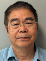 Head-and-shoulders image of an Asian man with short dark hair and glasses wearing a blue shirt against a plain gray background