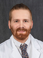Dr. Peter McCaffrey Professional headshot shows a man wearing a white lab coat and patterned tie against a dark gray background.