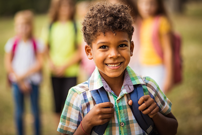 Young boy with curly hair in a plaid button-down shirt wearing a blue backpack
