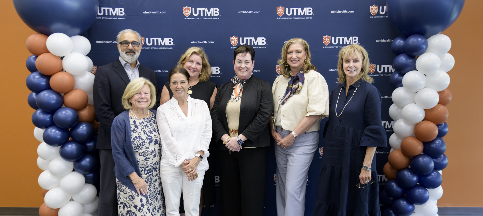 Seven people stand in two rows in front of a UTMB‑branded backdrop, flanked by balloon columns in navy, white, and orange.