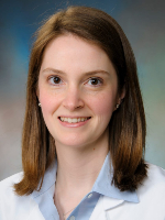 Dr. Julia W. Tripple Professional headshot shows a woman wearing a white coat and light blue collared shirt against a blue-gray studio background..