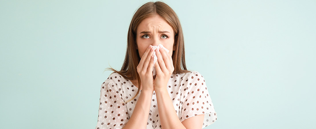 A person holds a tissue to the nose while standing against a light-colored background, illustrating symptoms commonly associated with seasonal allergies such as congestion or sneezing