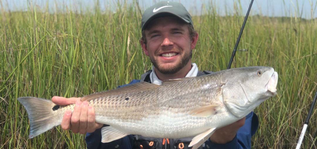 Person holding a redfish caught while fishing in warm coastal waters, with hands, fishing line, and seawater visible