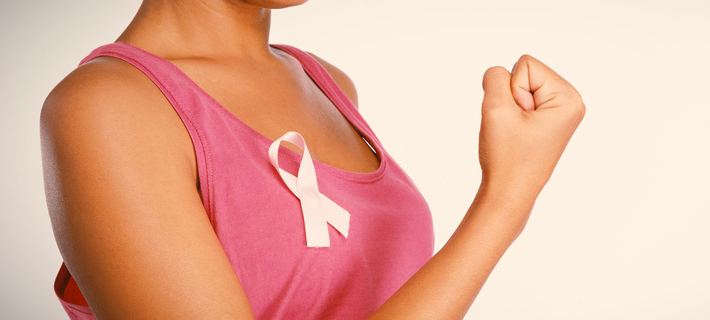Woman wearing a pink sleeveless top with a pink breast cancer awareness ribbon pinned to the chest, raising a clenched fist to symbolize strength, hope, and support for breast cancer awareness and screening