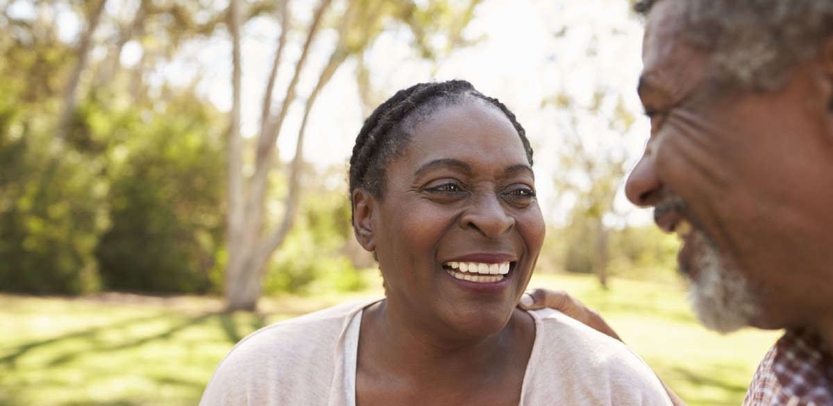 Smiling middle‑aged to older couple outdoors in a park, laughing together in sunlight, representing healthy aging and the importance of preventive care like colon cancer screening