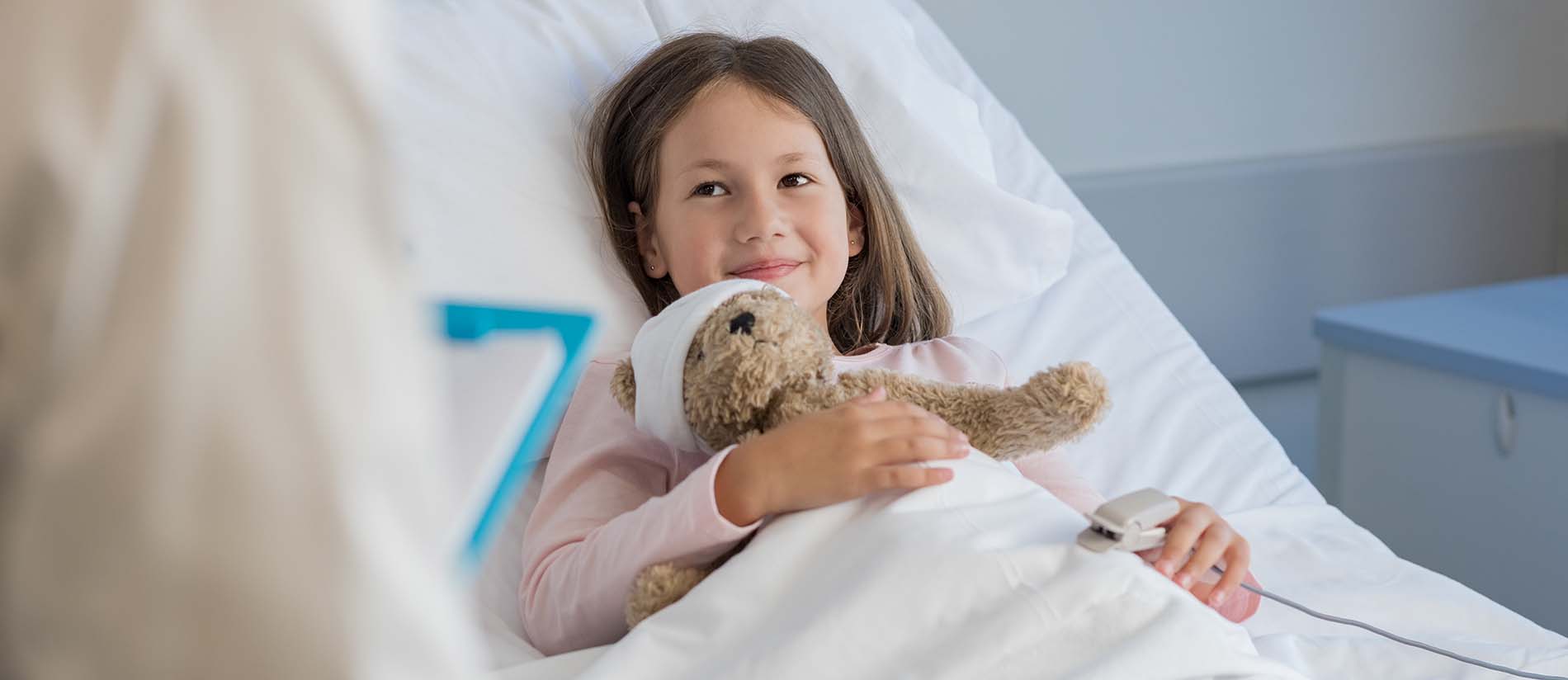 girl hold teddy bear in hospital bed