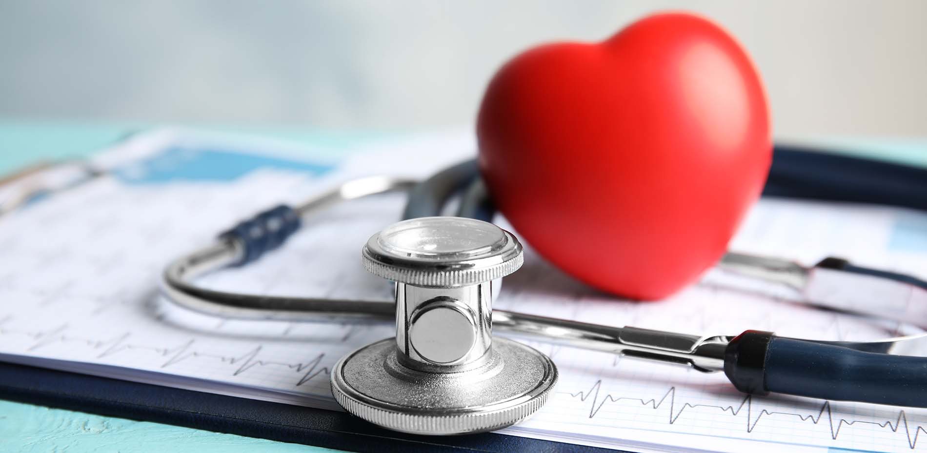 A red heart model rests beside a stethoscope on top of a sheet showing an electrocardiogram printout, symbolizing heart health and cardiac care