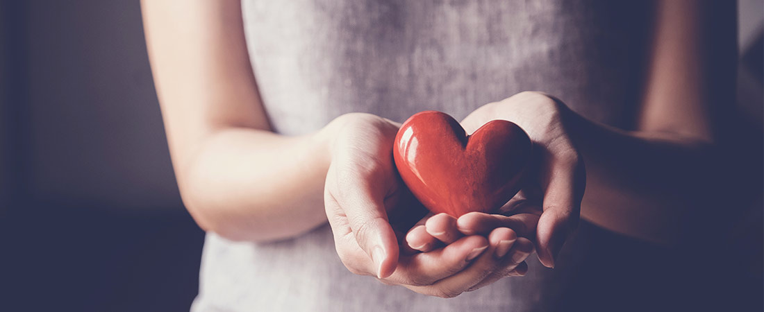 Person holding a red heart in their hands, symbolizing heart health and awareness