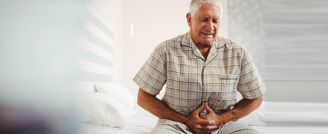 Person sitting on a bed holding the abdomen in a bedroom setting