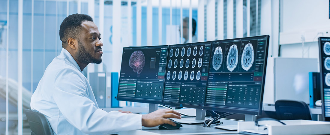 Clinician in a medical lab coat reviews multiple brain scan images on large computer monitors in a clinical setting, illustrating neurological evaluation and epilepsy care