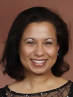Head-and-shoulders shot of a woman with dark hair and a brown blouse against a brownish studio backdrop